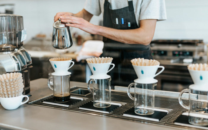 En barista häller vatten för hand över kaffefilter i en modern kaffebutik